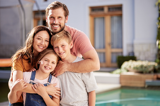 Happy family, relax outside house and outdoor with children, mom and dad smile with love by pool together. Portrait of mother, father and young kids hug together outside a modern home summer bonding