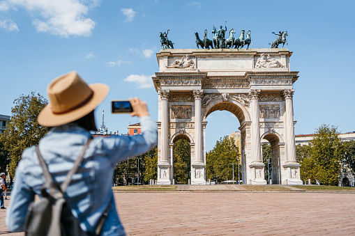 Beautiful young woman taking a picture of Arch of Peace in Milan, Italy.