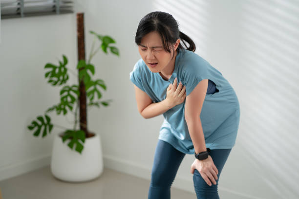 asiatische frau, die an brustschmerzen leidet, während sie zu hause im wohnzimmer trainiert. - gasping stock-fotos und bilder
