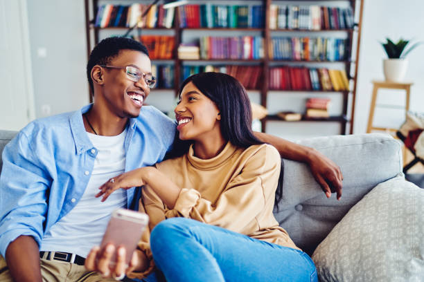 istock Satisfied black marriage resting at comfortable sofa enjoying weekend recreation in cozy home apartment, prosperous couple in live talking and laughing durians social networking via cellphone 1457094547