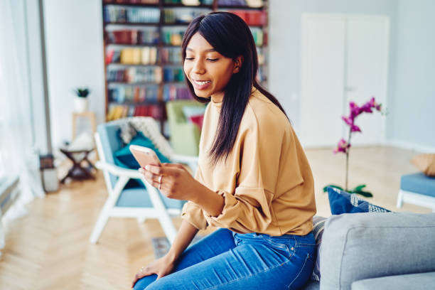 istock Pretty black female millennial typing text for sending mobile sms during web communication in loft apartment, attractive Generation Y with dark skin updating notification for smartphone application 1457094567