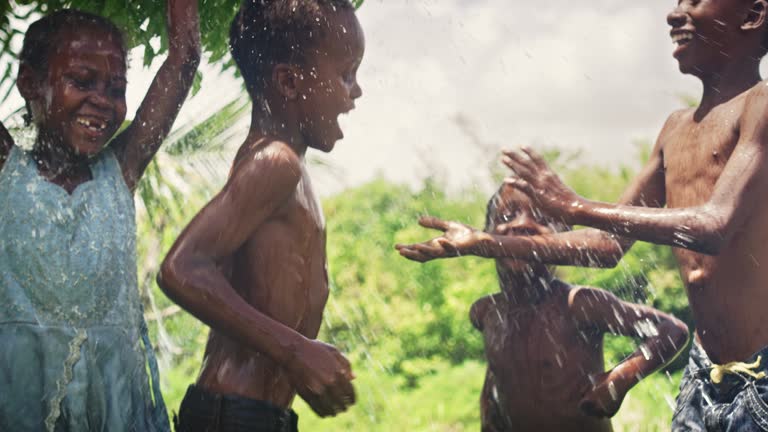 Group of African Kids Jumping and Laughing when Water Gets Poured on Them. Happy and Innocent Black Children Playing and Enjoying the Blessing of Rain Water After Long Drought. Pan Shot