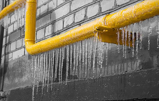 A yellow icy pipe with gas on the background of a gray wall.