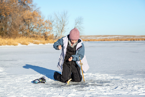 Young girl who has just caught a perch while ice fishing on a beautiful winter day. The fish is just coming out of the hole in the ice.