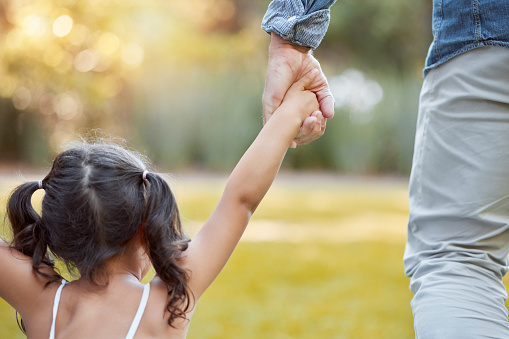 Holding hands, care and girl with father in a park with safety, support and security. Walk, trust and back of a child with dad in a backyard, field or nature in countryside for quality outdoor time