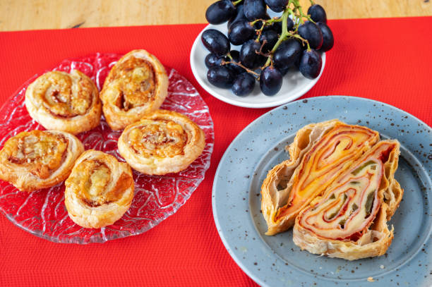 istock Salty rolled pastry with ham, cheese and sesame seed on two plate, dark grapes on red. 1457109720