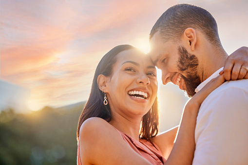 Sunset, romance and love with a couple hugging outdoor while happy dating in nature together. Sky, view and date with a young man and woman embracing while romantic bonding outside in summer