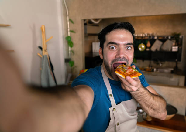 happy chef selfie for photo by mobile phone and eat delicious home made italian cheese sausage mushroom pizza after cook in kitchen of restaurant stock photo