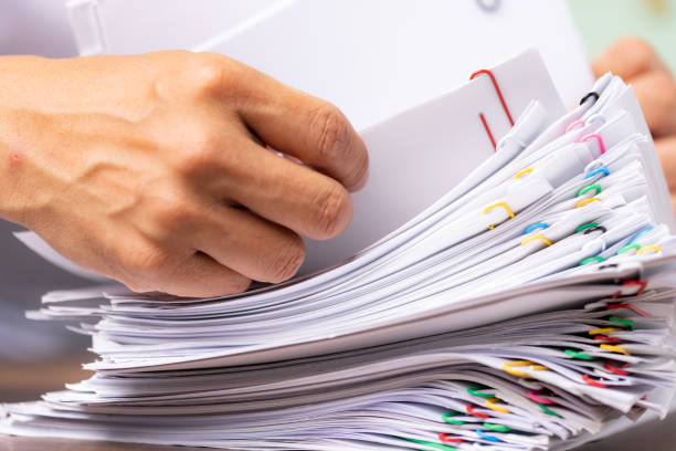 istock hands of a man in a white shirt searching for contract agreement documents in Stack of Group report papers clipped in color clips in fair light, business, legal law and education concept. 1457110681