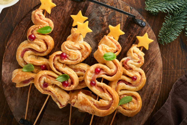 istock Christmas or New Year appetizer. Christmas tree shape puff pastry buns with cheese and ham. Group of Christmas tree shapes on wooden board. Festive idea for Christmas or New Year dinner. Top view. 1457112952