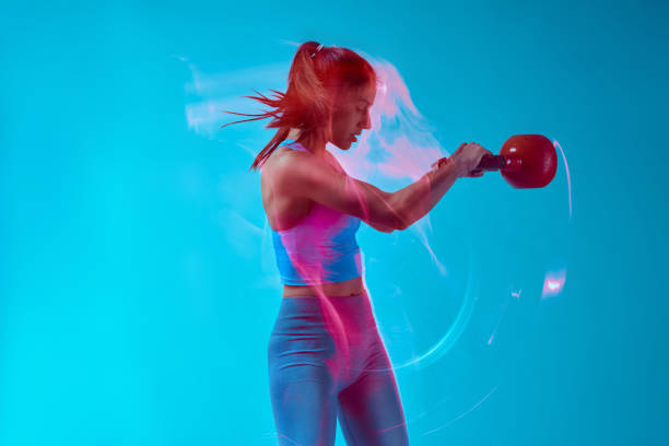 Un bodybuilder femminile che solleva kettlebell in studio. Cattura del movimento a lunga esposizione. - foto stock