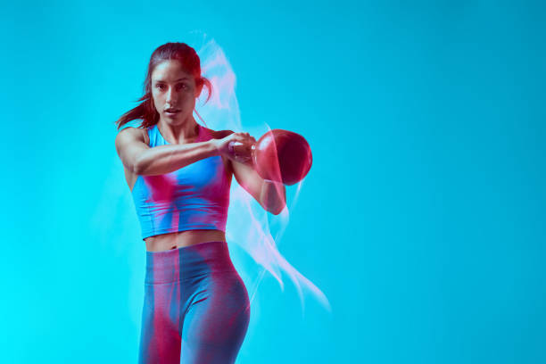 Un bodybuilder femminile che solleva kettlebell in studio. Cattura del movimento a lunga esposizione. - foto stock