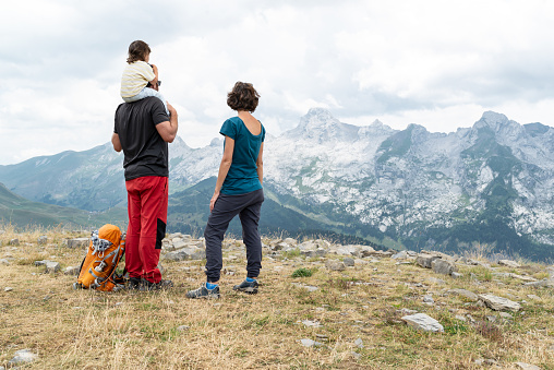 Rear view of man with her little daughter on shoulder and his partner looking at Aravis mountain range  in French Alps.