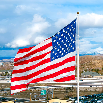 Aerial view of a Large American Flag in the Winter with rural farmland, snow capped mountains and a dramatic sky in the background.