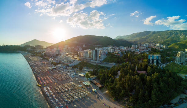 panorama della spiaggia con ombrelloni, lettini e persone che si rilassano nella città di becici vicino al mare adriatico sullo sfondo del cielo soleggiato - budva foto e immagini stock