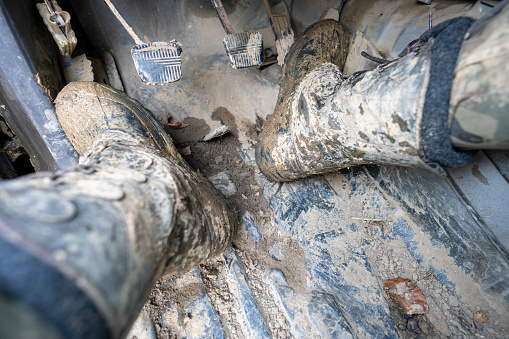 Close-up of a man's legs in military camouflage with trekking boots soiled in mud in the car