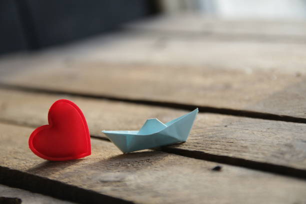 Red heart on a wooden background and paper boat. Place for text. Valentine. stock photo