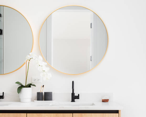 A bathroom with a wood cabinet and gold circular mirrors.