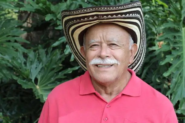 A senior man in his sixties is wearing a traditional Colombian hat. He has white hair and wears a mustache.