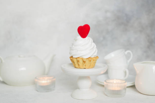 a cake with red heart and teapot, cups, candles on a gray background.
