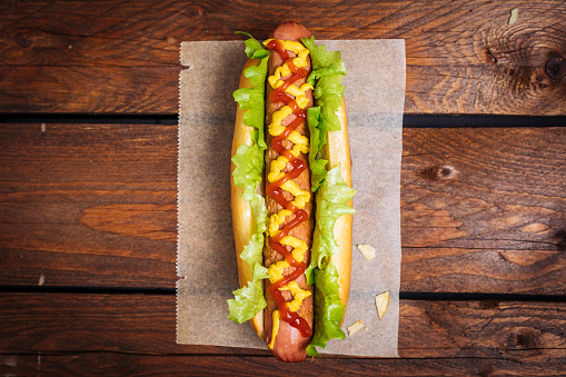 Hot Dog sausage and bun with ketchup and mustard sauce and lettuce and potato chips on Wooden Background
