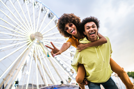 Multiracial young couple of lovers dating at the ferry wheel in the amusement park - People with mixed races having fun outdoors in the city- Friendship, relationship and lifestyle concepts
