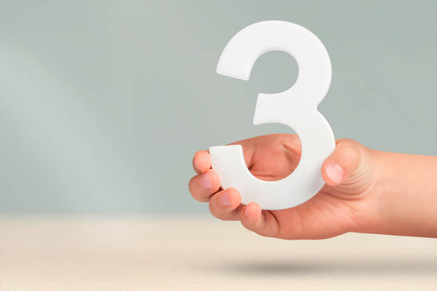 istock Number three in hand. Hand holding white number 3 on blurred background with copy space. Concept with number three. 3 percent, birthday 3 years, third grade, triple 1457142282