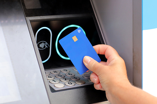 female hand with card by ATM. hand with credit card withdrawing money from ATM using NFC contactless wifi system. Wireless authentication and data transmission security in finance and banking