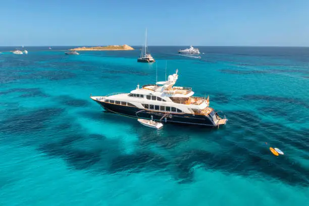 Photo of Aerial view of luxury yacht on blue sea at sunny day in summer. Sardinia, Italy. Aerial view of speed boats, yachts, sea lagoon, shore, transparent water, sky. Top view from drone. Tropical seascape
