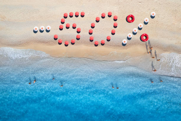 istock Creative text - 50% made from colorful umbrellas on sandy beach and blue sea with waves at sunny day. Aerial view of sea coast and text. Summer sale and discount. Background. Top view of clear water 1457146846