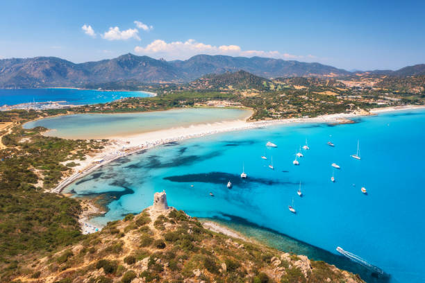 Aerial view of beautiful sandy beach, old tower on the hill, sea bays, mountains at summer sunny day. Porto Giunco in Sardinia, Italy. Top view of blue sea with clear water, white sand, mountains stock photo