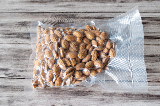 Vacuum-packed dried almond nuts on a wooden background. Plant-based diet, healthy fats, keto diet, lchf.