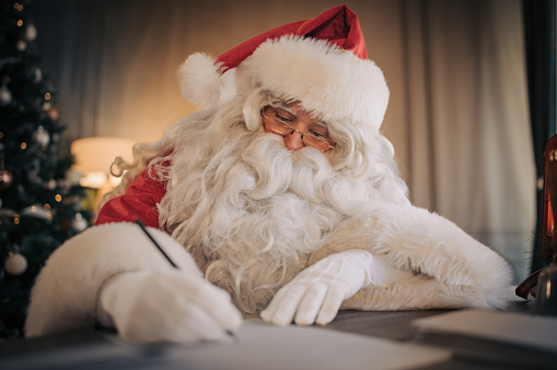 Santa Claus sitting at the desk and writing a letter at home.