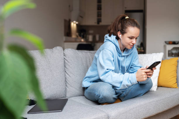 istock Woman messaging online using her cell phone while sitting in lotus pose on sofa at home. 1457148942