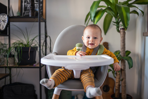 Cute baby boy sitting in his high chair and waiting for his lunch.