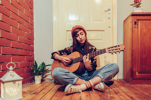 Relaxed woman at home is drinking wine and playing the guitar