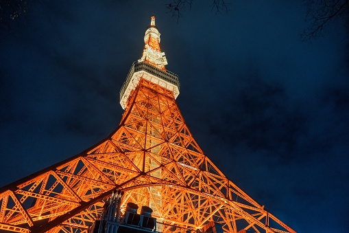 Low angle close up shot of tall architecture tourist attraction Tokyo tower with lights up and the background of the evening sky.\n\nA moody shot of the cityscape or city landscape of modern Tokyo city at night with lights, Tokyo tower or Japan Radio Tower, a communications and observation tower in the Shiba-koen district of Minato, Tokyo, Japan.