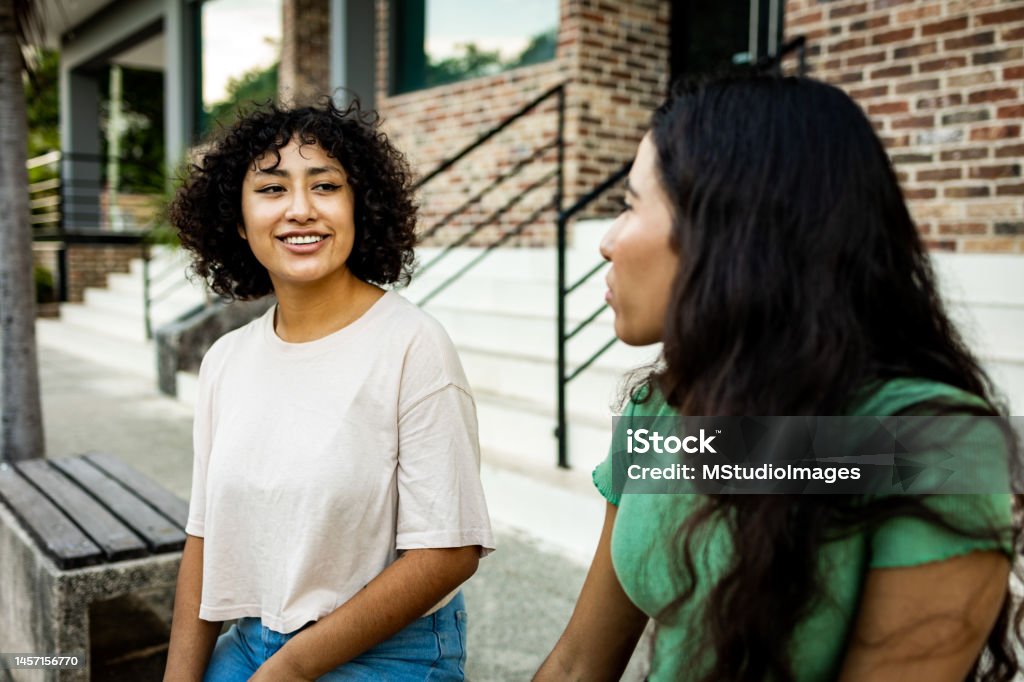 Two women sitting on the bench and talking Two young women sitting outdoors and talking Discussion Stock Photo