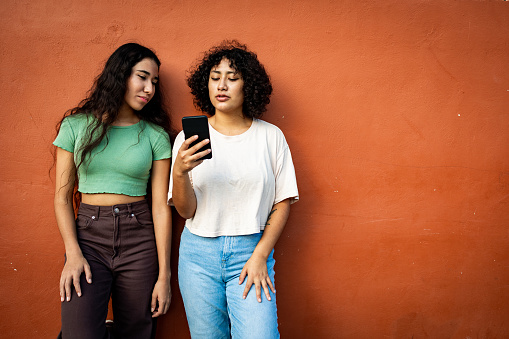 Two young women standing and using mobile phone