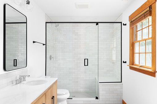 A beautiful luxury, modern bathroom with a light wood cabinet, walk-in shower with marble subway tiled walls, and black faucets and hardware.