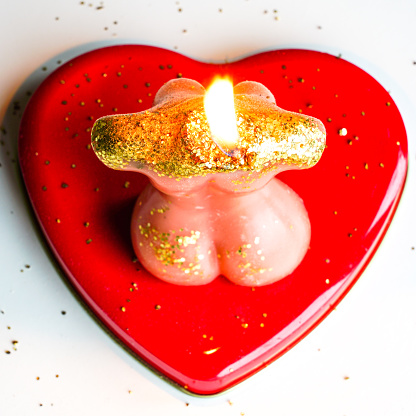 A burning candle in the shape of a beautiful woman's body on a red heart-shaped pad, Valentines day concept