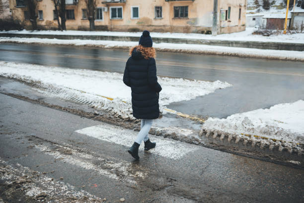 Woman dressed in coat and hat crosses the road at pedestrian crossing Woman dressed in coat and hat crosses the road at pedestrian crossing, which covered with dirty slush on winter day slippery unrecognizable person safety outdoors stock pictures, royalty-free photos & images