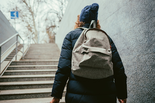 Rear view young woman wearing winter down jacket and backpack walks