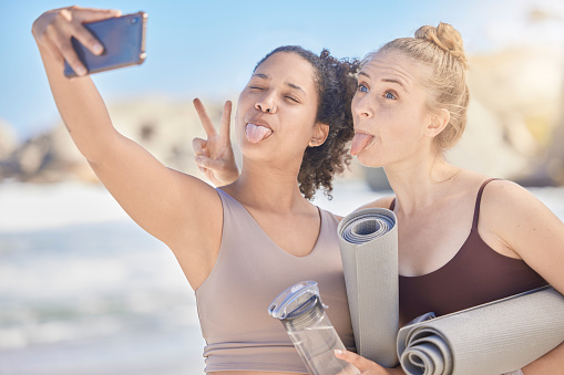Happy face selfie, yoga and women with yoga mat exercise at the beach for fitness workout, spiritual health and zen meditation. Fun with a friend, stress relief and pilates wellbeing workout training