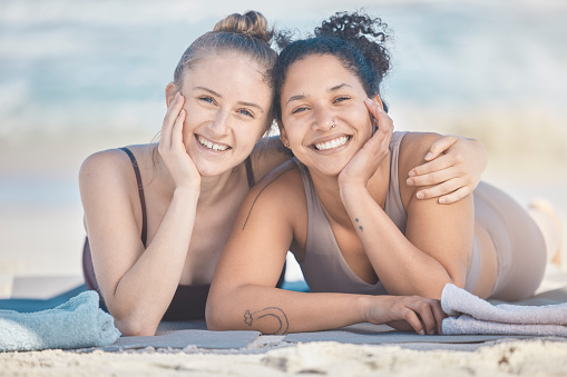 Friends, beach and diversity with a black woman and happy friend lying on the sand by the sea or ocean in nature. Face, smile and summer with a female and friend by the water to relax on vacation