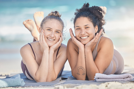 Friends, smile and beach happiness with women together on vacation, holiday and travel while lying on sand, bonding and enjoying freedom. Face portrait of lesbian couple outdoor at sea for summer fun