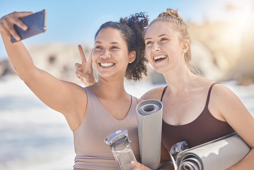 Woman, friends and phone selfie in yoga with smile for healthy exercise, training or workout at the beach. Women in fitness taking a photo with mobile smartphone for happy moments together outside