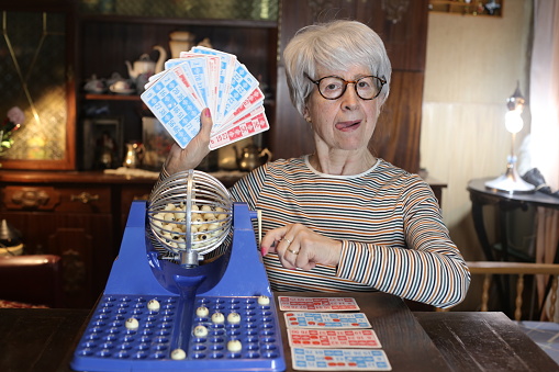 A cute senior woman in her sixties is playing some bingo. She has short gray hair and wears eyeglasses.
