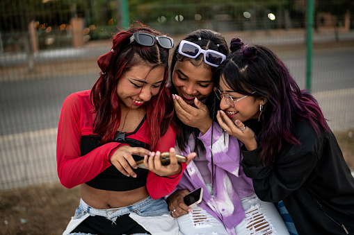 Female friends having fun while watching a video on mobile phone outdoors