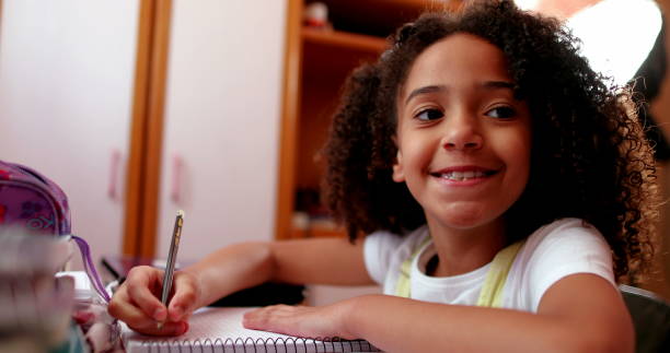 Cute schoolgirl smiling at camera while doing homework stock photo